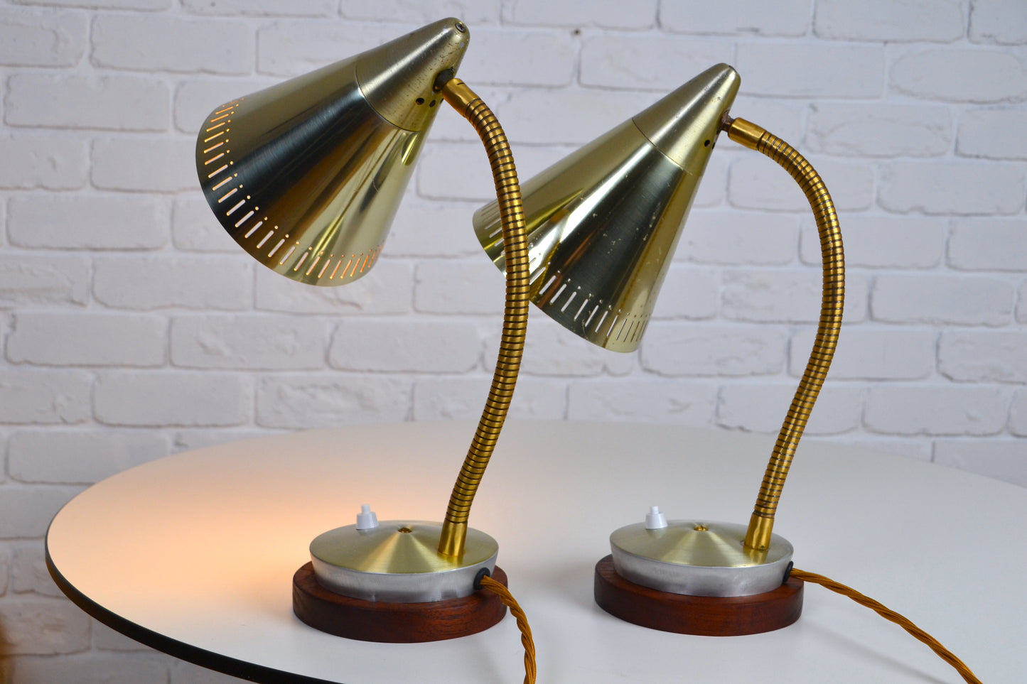 Pair of vintage-style brass desk lamps on a white surface with a white brick wall background.