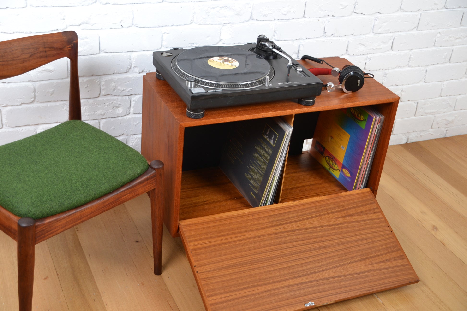 Turntable with records on a wooden cabinet next to a green-seat chair.
