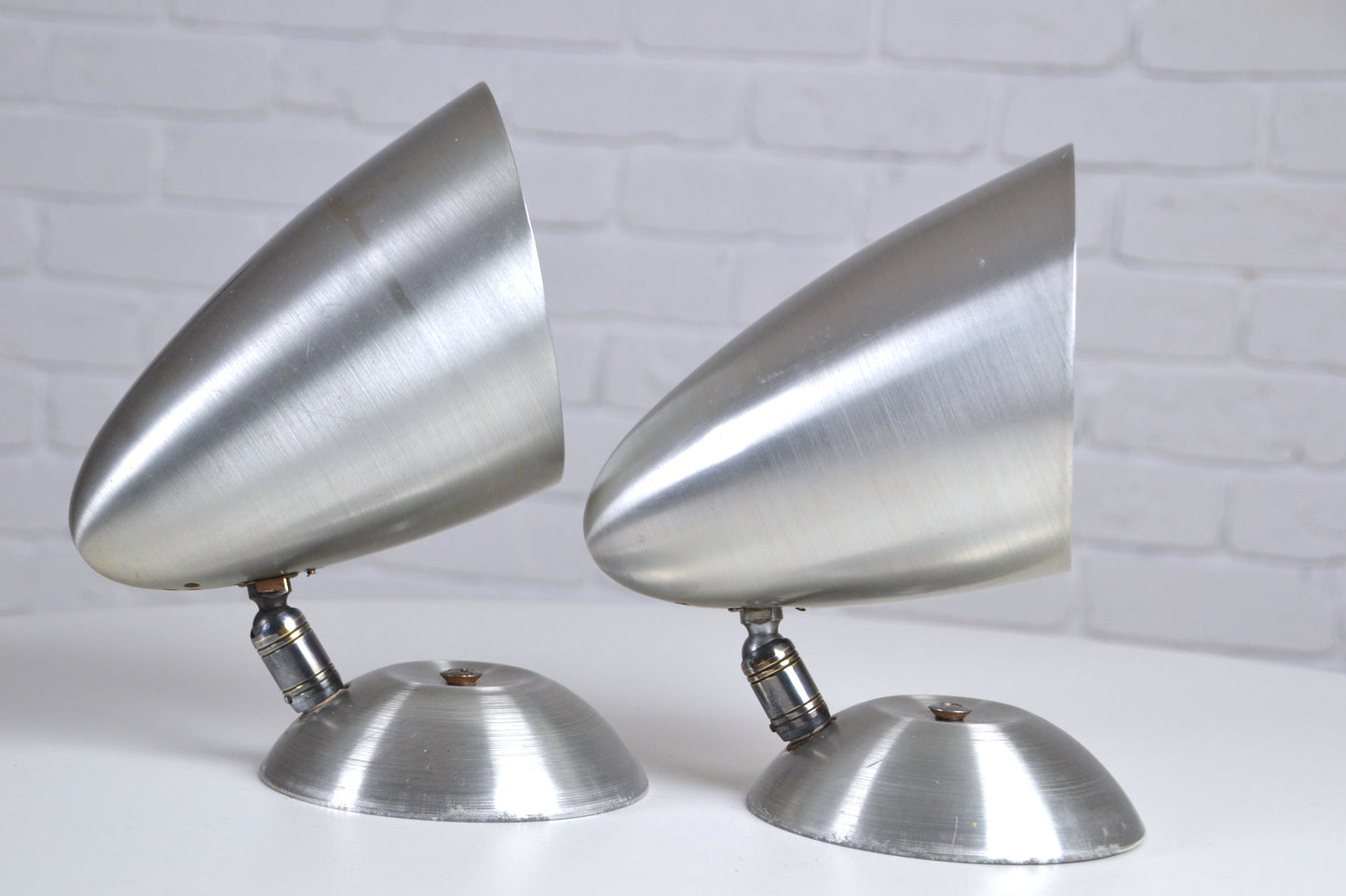 Two metallic cone-shaped objects on a white surface with a light gray brick wall background.
