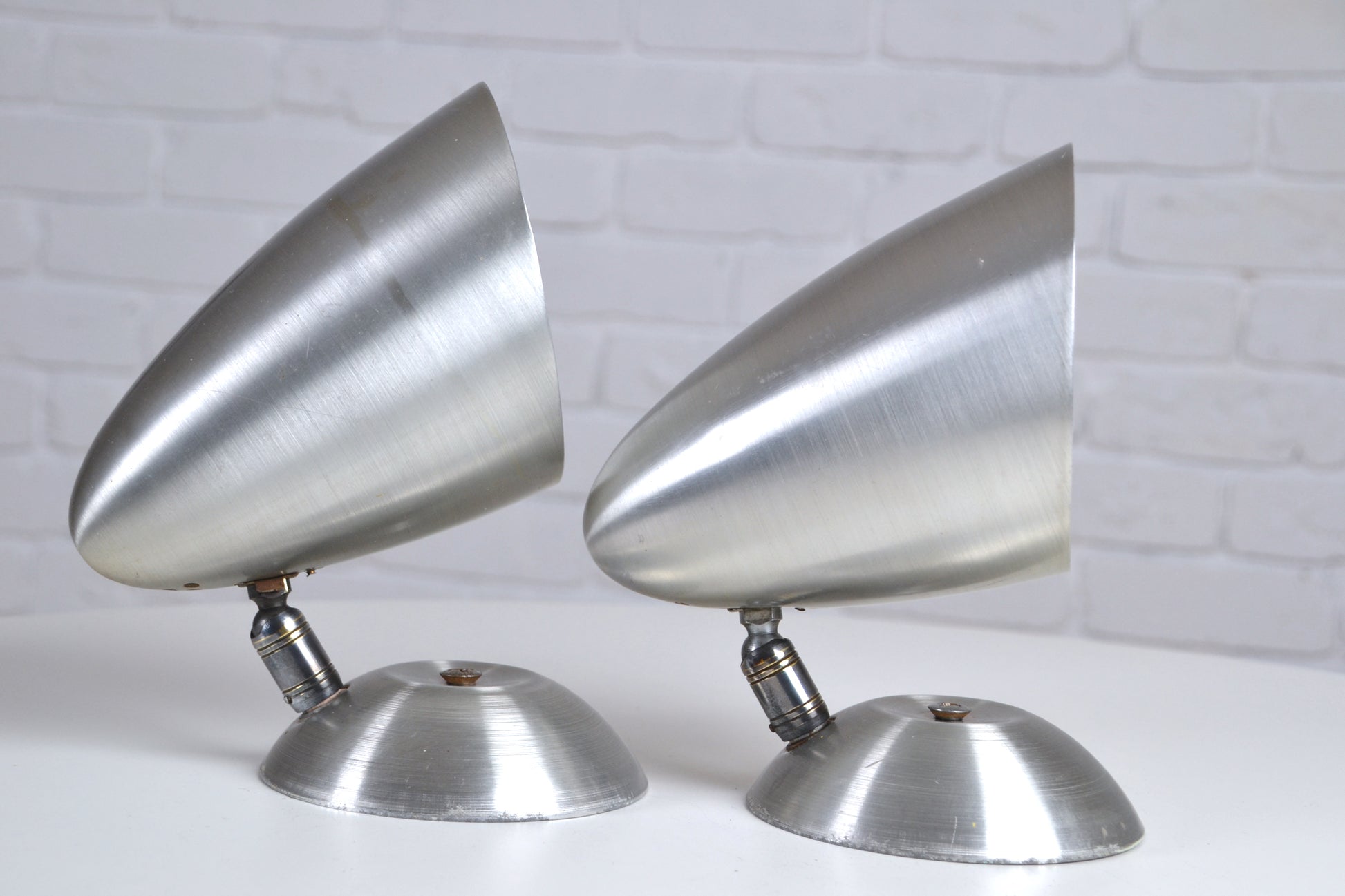 Two metallic cone-shaped objects on a white surface with a light gray brick wall background.