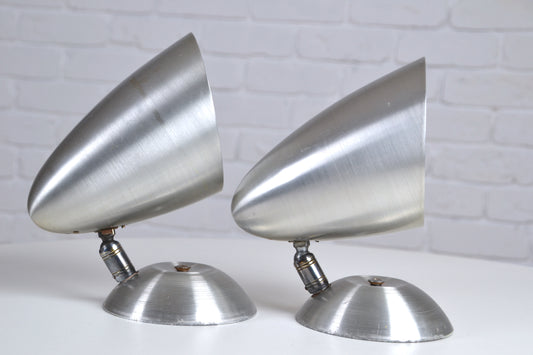 Two metallic cone-shaped objects on a white surface with a light gray brick wall background.