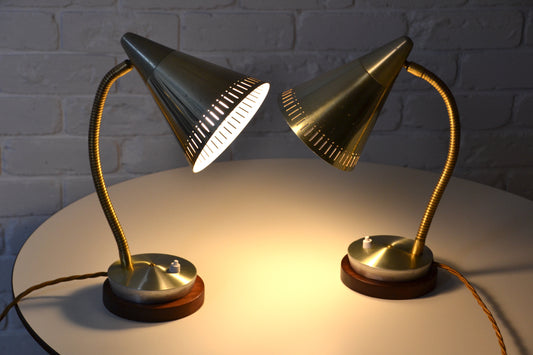Two vintage mid century desk lamps on a white surface with a brick wall background.